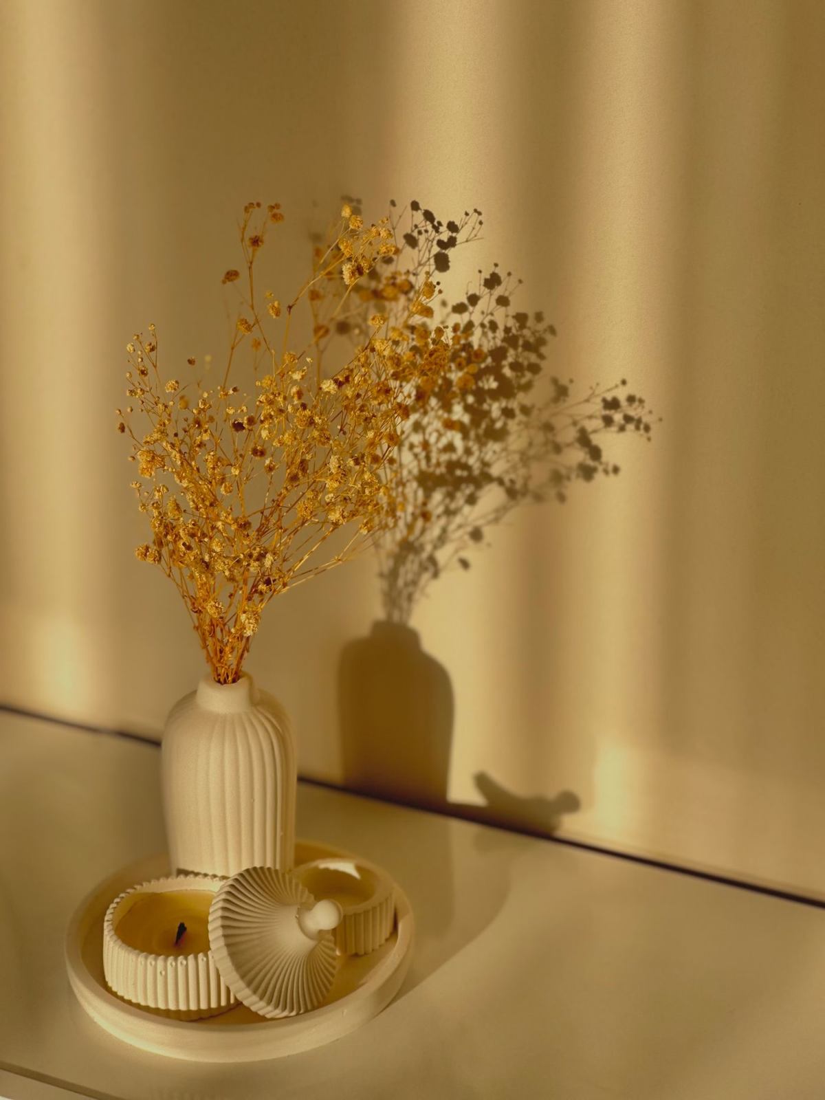 Droogbloemen in een geribbelde vaas en kaarsen in warm strijklicht